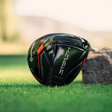 Taylormade Stealth driver lying on grass and resting on a rock with the sole of the Stealth Driver showing.