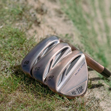 Three, TaylorMade Hi-Toe 3 Wedges lying on a  grass bank showing three different specs of bounce. On the right the 60 / 13. Middle 60 / 10 and left the 60 / 07 