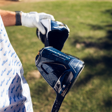Callaway Golf Paradym Driver being pulled out of driver headcover by a golfer. At an angle that shows of the back of the club head on a grass background