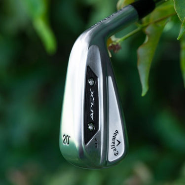 Callaway Apex UT 24 Golf Iron being held so the sole and back of the club head are visible. On a green background with some leaves in the background