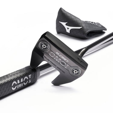 Mizuno OMOI Putter in Intense Black ION lying on the ground on top of a shaft and grip of another OMOI 6 with the OMOI 6 headcover in the background